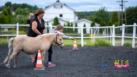 Barn kaster en ring fra hesteryggen med en voksen ved siden av på Hjørgunn