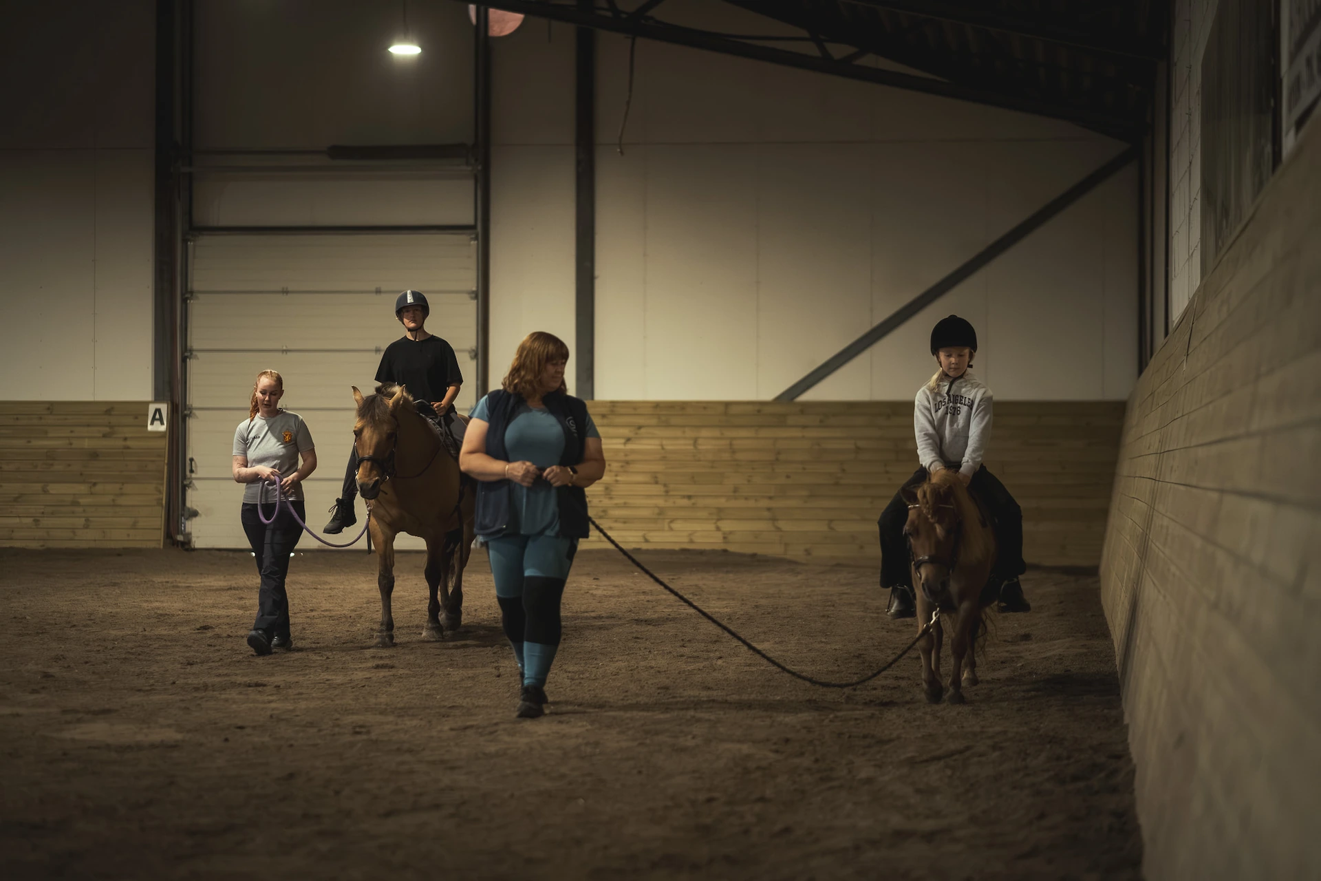 Barn rir i ridehallen med voksne tett på
