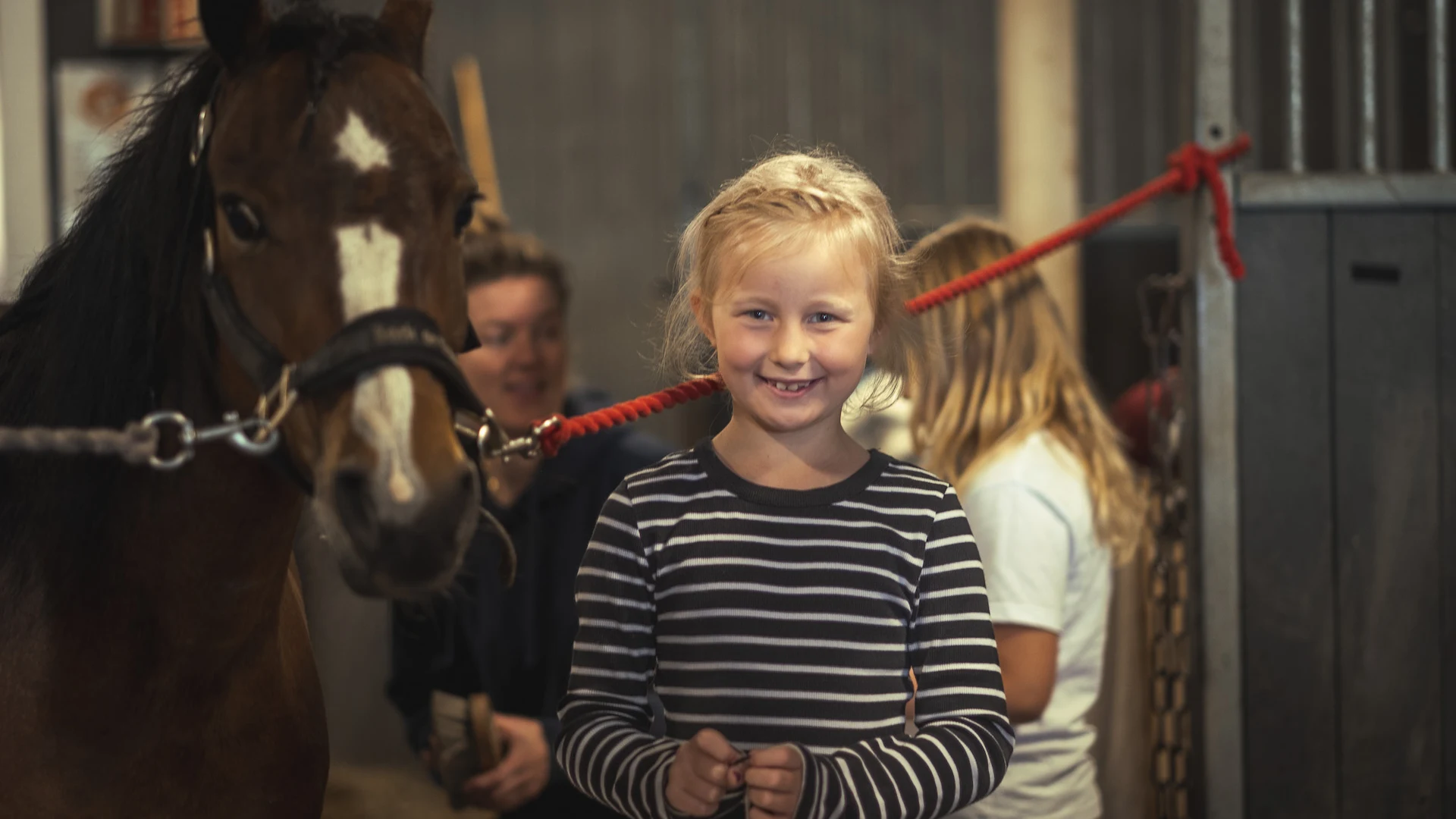 Smilende barn sammen med hest i stallen på Hjørgunn